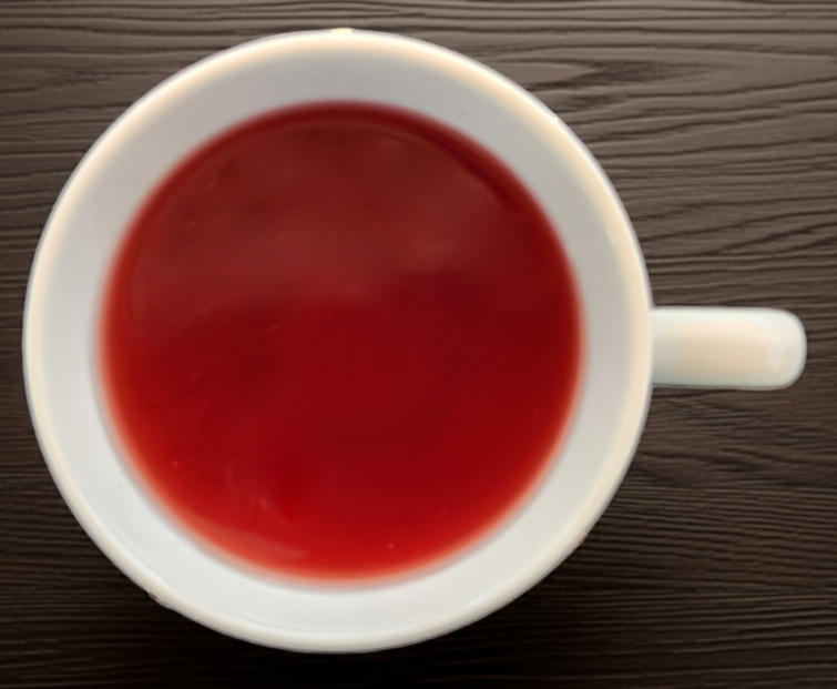 White mug filled with red liquid on a dark wooden surface